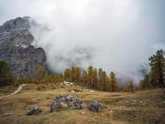 Remote mountain landscape with fog-shrouded rocky peaks and autumn-colored trees at Erjavčeva mountain hut.