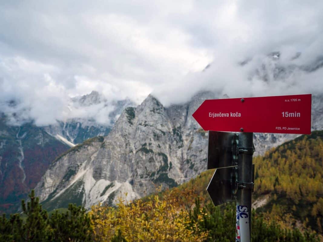 Remote mountain landscape with fog-shrouded rocky peaks and autumn-colored trees at Erjavčeva mountain hut.